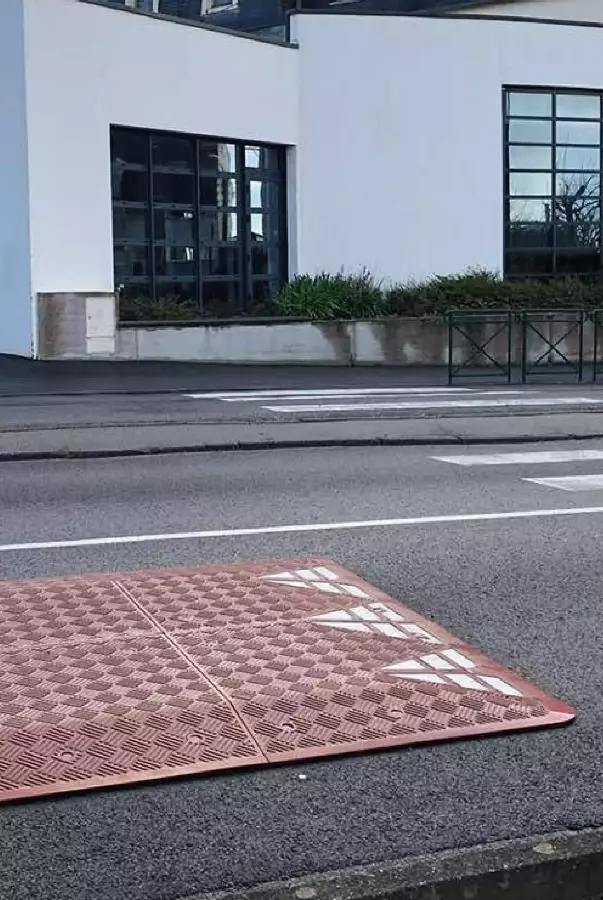 A piece of red and white rubber speed cushion is placed next to the crosswalk