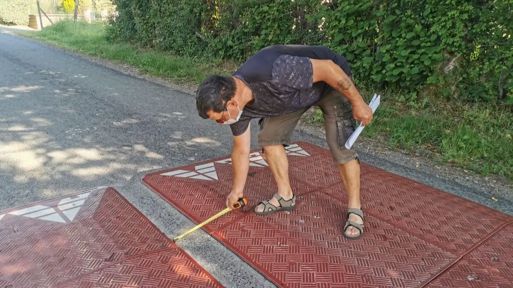 A man is measuring the distance between two red rubber speed cushions.