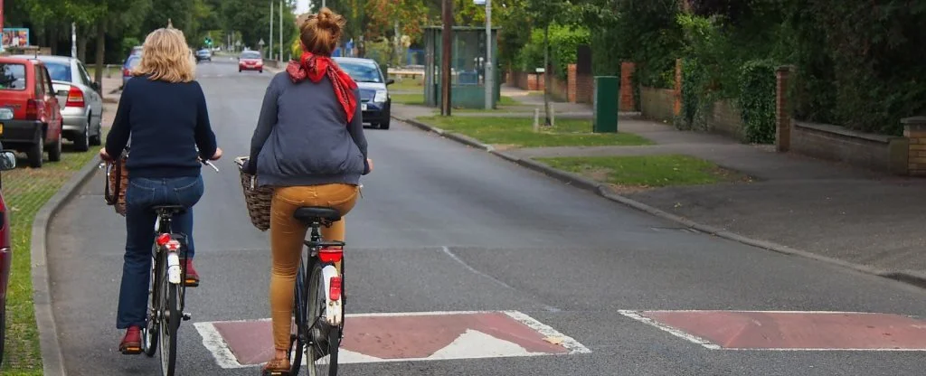Two cyclists are passing by two red and white speed cushions made of concrete.