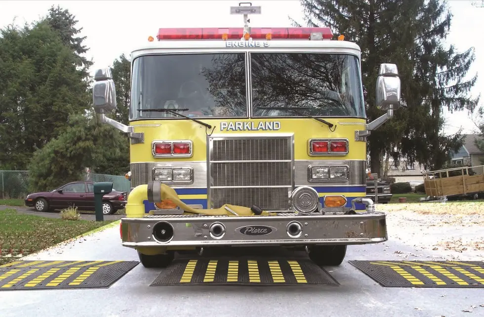 An emergency vehicle is passing over black and yellow speed cushions.